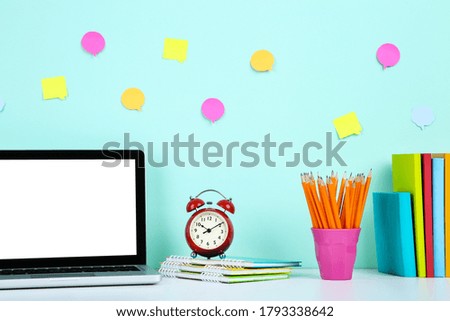 Laptop computer with notepads, pencils and alarm clock on blue background