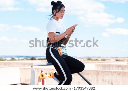 Asian woman with sportswear and skateboard using her smartphone