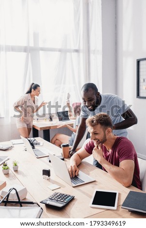 Selective focus of multiethnic businessmen using laptop near colleagues in office