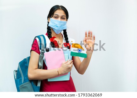 Independence Day (15 august) - happy Indian teenager girl in school uniform with braided hair  holding books, waving hands, wearing protective surgical face mask of Indian flag. Royalty-Free Stock Photo #1793362069