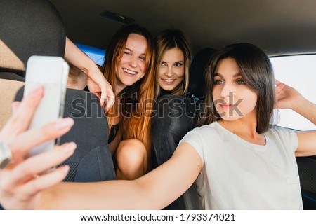Three happy smiling female travelers posing together for mobile photo about wonderful road trip, selfie with friends, happy memories.