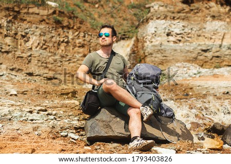 Handsome young male backpacker in sunglasses resting in mountains and rocks.