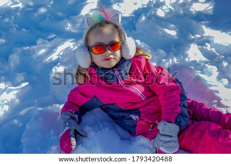 Young girl with sunglasses sitting on the snow place. Winter time