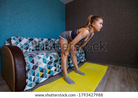 Young woman in black sportswear is practicing yoga, standing in the front bend pose, performing an exercise, athletic girl exercising at home or in a yoga studio with gray walls, body stretching