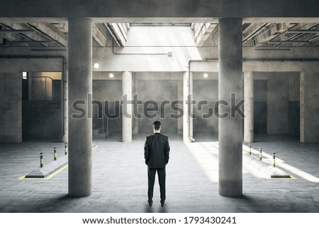 Businessman standing in underground parking interior with columns. Urbanization and transport concept.