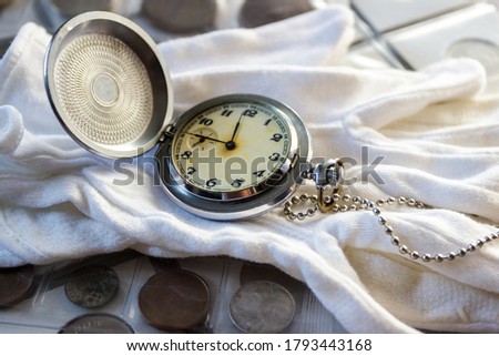 Different old collector's coins with a pocket watch, soft focus background