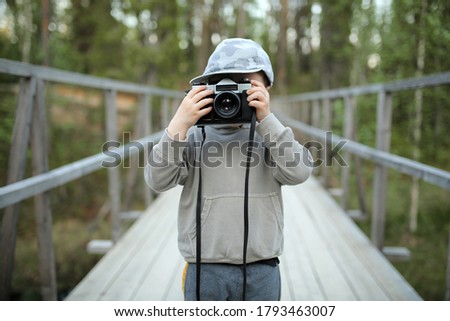 Little boy with an old camera takes pictures in the open air. A child takes a photo with a vintage retro camera. on a wooden bridge