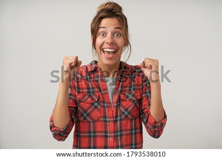 Agitated young attractive brunette woman with natural makeup raising emotionally her hands while looking excitedly at camera, standing over white background