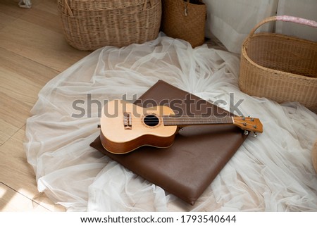 A small guitar is placed on a thin white cloth on the floor.