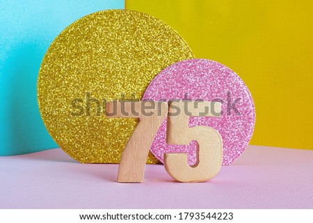 the gold number “75” on a multicolored blue-yellow-pink background and two shiny gold and pink circles. happy birthday greeting card concept.
