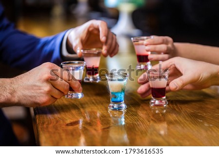 Cocktail at the nightclub. Group friends tequila shot glasses in bar. Male hands glasses of shot or liqueur. Friends drink shot or liqueur. Five glasses of alcohol.Tequila shots, vodka, whisky, rum.