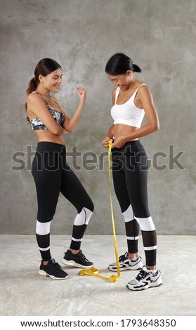Two beautiful young Asian women measuring their waist at the gym. Happy female friends spending their free time at the sport centre 