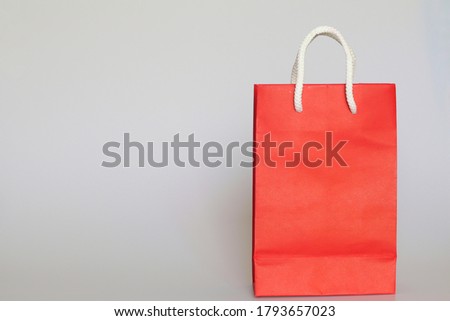Red paper shopping bag with handle made by white rope​ and​ copy​ space​ on​ left​ side​ isolated on grey​ background​ for​ edit​ or​ montage​.