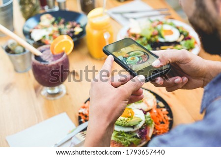 Influencer man eating brunch while making video and photos of dish with mobile phone in trendy bar restaurant - Healthy lifestyle, technology and food trends concept - Focus on man hand Royalty-Free Stock Photo #1793657440