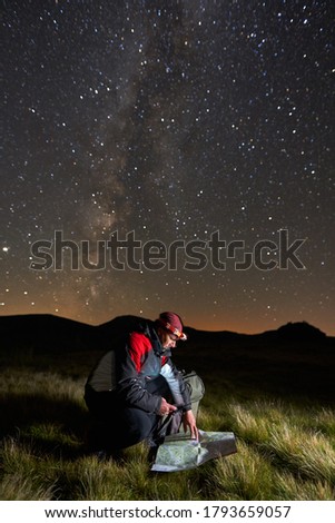 Man with backpack and map hiking in the mountains under Milky Way starry sky at night