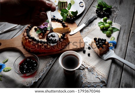 Big round cheese cake with black currant and a cup of coffee on a wooden grey table. 