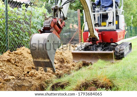 Workman using a mini digger to excavate a hole for water pipes in the garden. Czech republic, Europe. Royalty-Free Stock Photo #1793684065