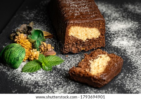 Chocolate cake on black background, icing sugar and decorative herbs