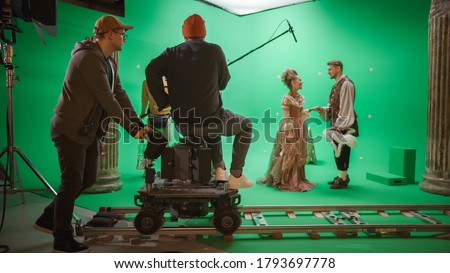On Film Studio Set Shooting History Movie Green Screen Scene. Moving Cameraman on Railway Trolley Shooting Two Costumed Actors while Director Controls Process. Crew on Big Budget Filmmaking