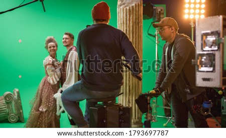 On Film Studio Set Shooting Historical Movie Green Screen Scene. Cameraman on Railway Trolley Shooting Two Costumed Actors while Director Controls Process. Professional Crew on Big Budget Filmmaking