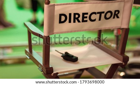 On Film Studio Set Close Up Shot of Empty Director's Chair. In the Background Professional Crew Shooting Green Screen Scene with Actors for History Movie.