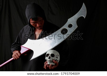 Happy Halloween day devil ghost killer horror fear concept. Reaper demon costume horror and scary holding red handle of big sharp knife and skull in black background. The vampire ghost people
