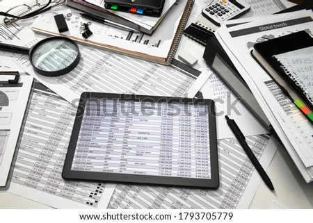 business office desk closeup - tablet computer with tables and graphs on the screen, financial reports, analysis and accounting, set of documents for bookkeeping