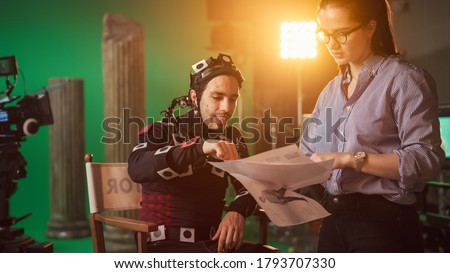 On Film Set: Prominent Female Director Explains Scene to Male Actor Wearing Motion Capture Suit and Playing Green Screen Scene in Superhero Movie. On Big Film Studio Professional Crew