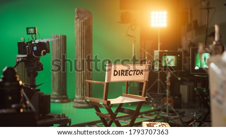 Film Studio Set with Focus on Empty Director's Chair. On the Studio Film Set with High End Equipment Professional Crew Shooting High Budget Movie Royalty-Free Stock Photo #1793707363