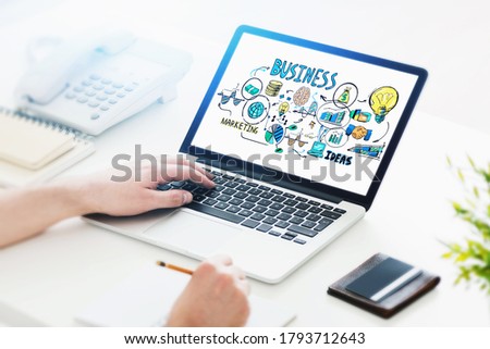 Hand of businessman using laptop at blurry office table with colorful business sketch on the screen. Toned image