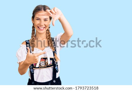 Beautiful caucasian woman with blonde hair wearing octoberfest traditional clothes smiling making frame with hands and fingers with happy face. creativity and photography concept. 