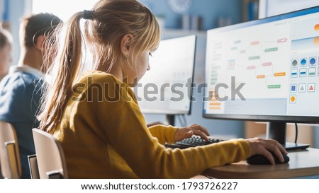 Elementary School Computer Science Classroom: Cute Little Girl Uses Personal Computer, Learning Programming Language for Software Coding. Schoolchildren Getting Modern Education. Over the Shoulder Royalty-Free Stock Photo #1793726227