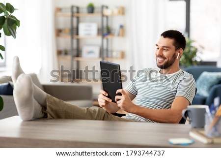 technology, remote job and lifestyle concept - happy smiling man with tablet pc computer and earphones resting feet on table at home office