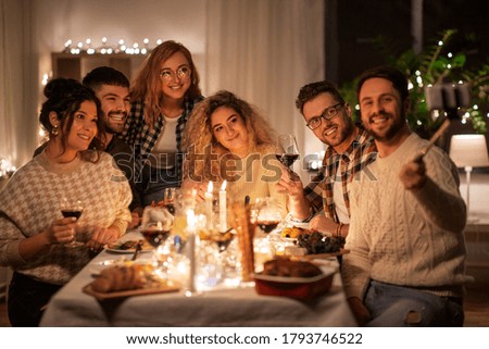 holidays, celebration and people concept - happy friends taking with smartphone on selfie stick at home christmas dinner party