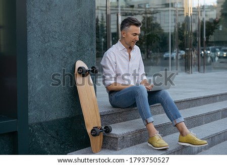 Handsome middle aged man working online, planning start up. Mature businessman using laptop outdoors. Portrait of successful freelancer typing on keyboard, sitting outdoors  