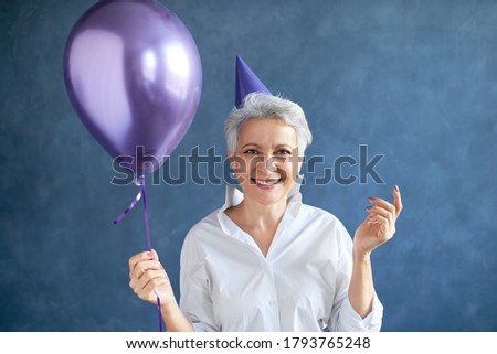 Isolated image of attractive successful mature businesswoman with short gray hair posing at blank studio wall with helium balloon, expressing positive emotions ar surprise party. People and lifestyle