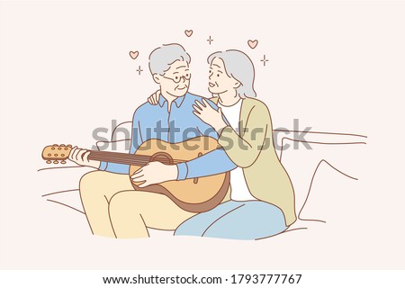 Couple, love, play, romance, music, recreation concept. Romantic old man and woman senior citizens pensioners sitting on couch together and playing guitar musical instrument at home. Happy retirement.