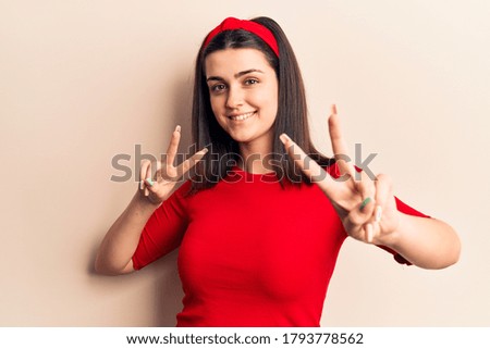 Young beautiful girl wearing casual t shirt and diadem smiling looking to the camera showing fingers doing victory sign. number two. 