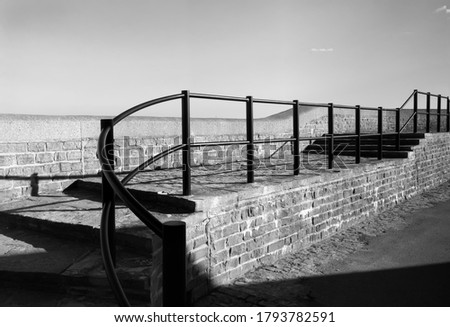 Black and white photograph of beautifully curving railings along a sea walk with a bright sky above.  