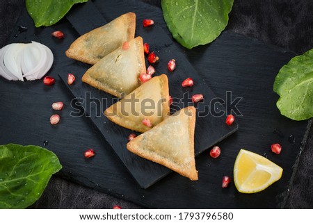 Veg Samosa - is a crispy and spicy Indian triangle shape snack which has crisp outer layer of maida filling of mashed potato, peas and spices. Served with fried green chilly, onion chutney ketchup. Royalty-Free Stock Photo #1793796580