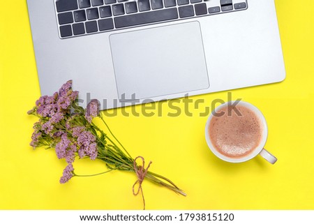 Holiday office desk composition - laptop, cup, bouquet of flowers on yellow table. Good morning concept
