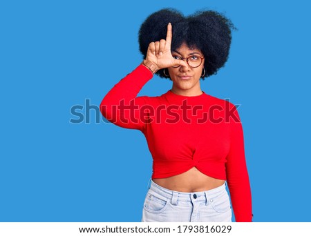 Young african american girl wearing casual clothes and glasses making fun of people with fingers on forehead doing loser gesture mocking and insulting. 