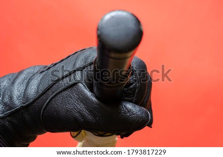 Hand in black leather glove holds an umbrella against coral background. Rain and wind protection accessory with black handle. Top view at an angle.