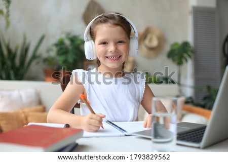 Smiling little girl in headphones handwrite study online using laptop at home, cute happy small child in earphones take Internet web lesson or class on PC.