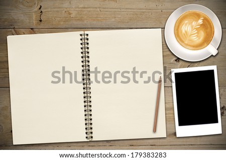An Open Vintage Sketchbook or Notebook with pencil, photo and latte art coffee on Old Wooden Table. 