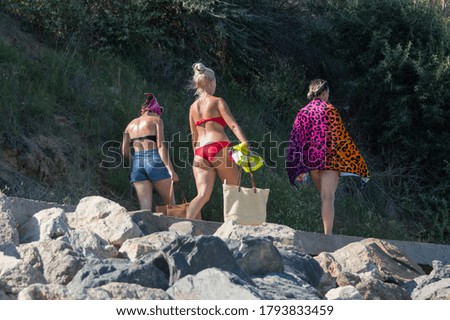 Girls in swimsuits walk on the seafront to the beach. Three attractive girls walking along seafront. Rear view. Lifestyle for youth and travel. The concept of summer vacation