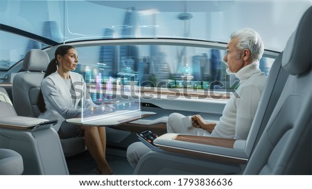 Casual Business Meeting Between Senior Male and Female inside a Futuristic Driverless Autonomous Car with Augmented Reality Presentation Interface. Self-Driving Van Driving on Downtown City Streets. Royalty-Free Stock Photo #1793836636
