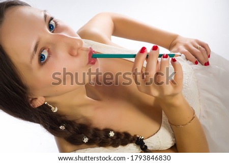 The woman took a pencil in her mouth. A woman dressed in a white dress braids
