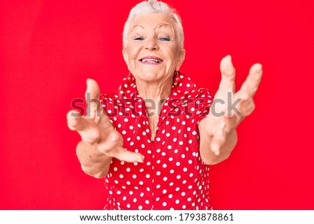 Senior beautiful woman with blue eyes and grey hair wearing casual summer clothes over red background looking at the camera smiling with open arms for hug. cheerful expression embracing happiness. 