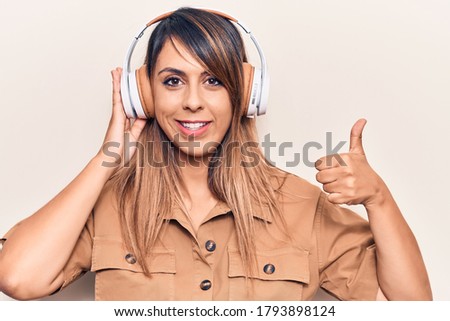 Young beautiful woman listening to music using headphones smiling happy and positive, thumb up doing excellent and approval sign 